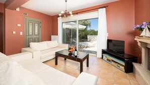 Una sala de estar con sofá, mesa de centro, televisor y vistas al exterior.