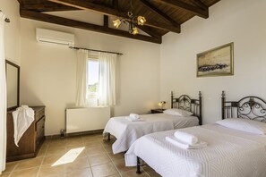 A bedroom with two beds, a radiator, a window with curtains, a painting on the wall, and a wooden ceiling.