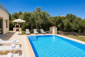 A swimming pool with lounge chairs and an umbrella, surrounded by stone tiles and greenery. - Villa Thalea - Two Bedroom Villa, Sleeps 4 (Lefkada)