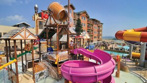 Ein Wasserpark mit einer großen, violetten Rutsche, einer hölzernen Spielanlage und einem Poolbereich.