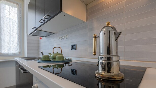 A modern kitchen with a stainless steel espresso machine, a green tea set, and a window with a geometric curtain. - Casa Gabel by Wonderful Italy (Torino)