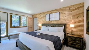 Une chambre avec un grand lit, des murs recouverts de panneaux de bois, un banc, une table de chevet et une fenêtre donnant sur des rochers et de la verdure.