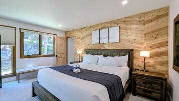 A bedroom with a large bed, wooden panel walls, a bench, a bedside table, and a window with a view of rocks and greenery.