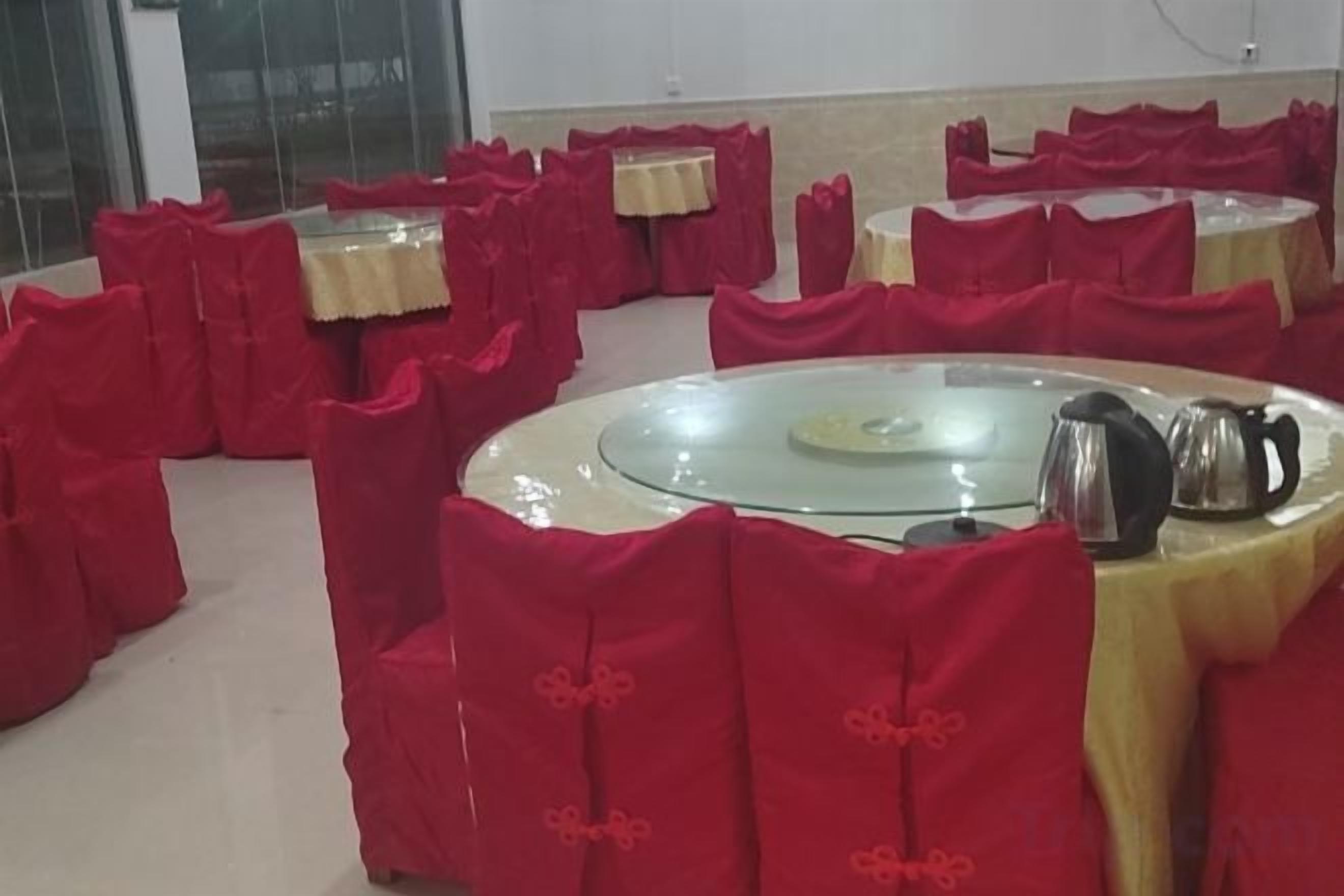 A room with round tables covered with red tablecloths and chairs, arranged in a circular pattern.