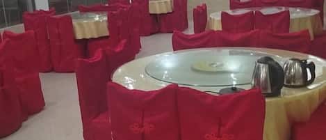 A room with round tables covered with red tablecloths and chairs, arranged in a circular pattern.