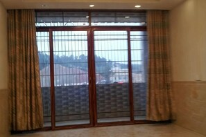 Una stanza con un'ampia porta vetrata scorrevole che dà su un balcone, una tenda decorata e un pavimento piastrellato.