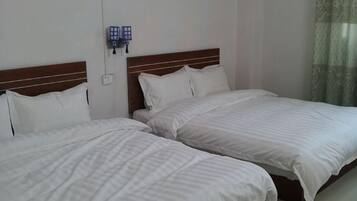 Two single beds with wooden headboards, white bedding, a wall-mounted phone, and a window with sheer curtains.