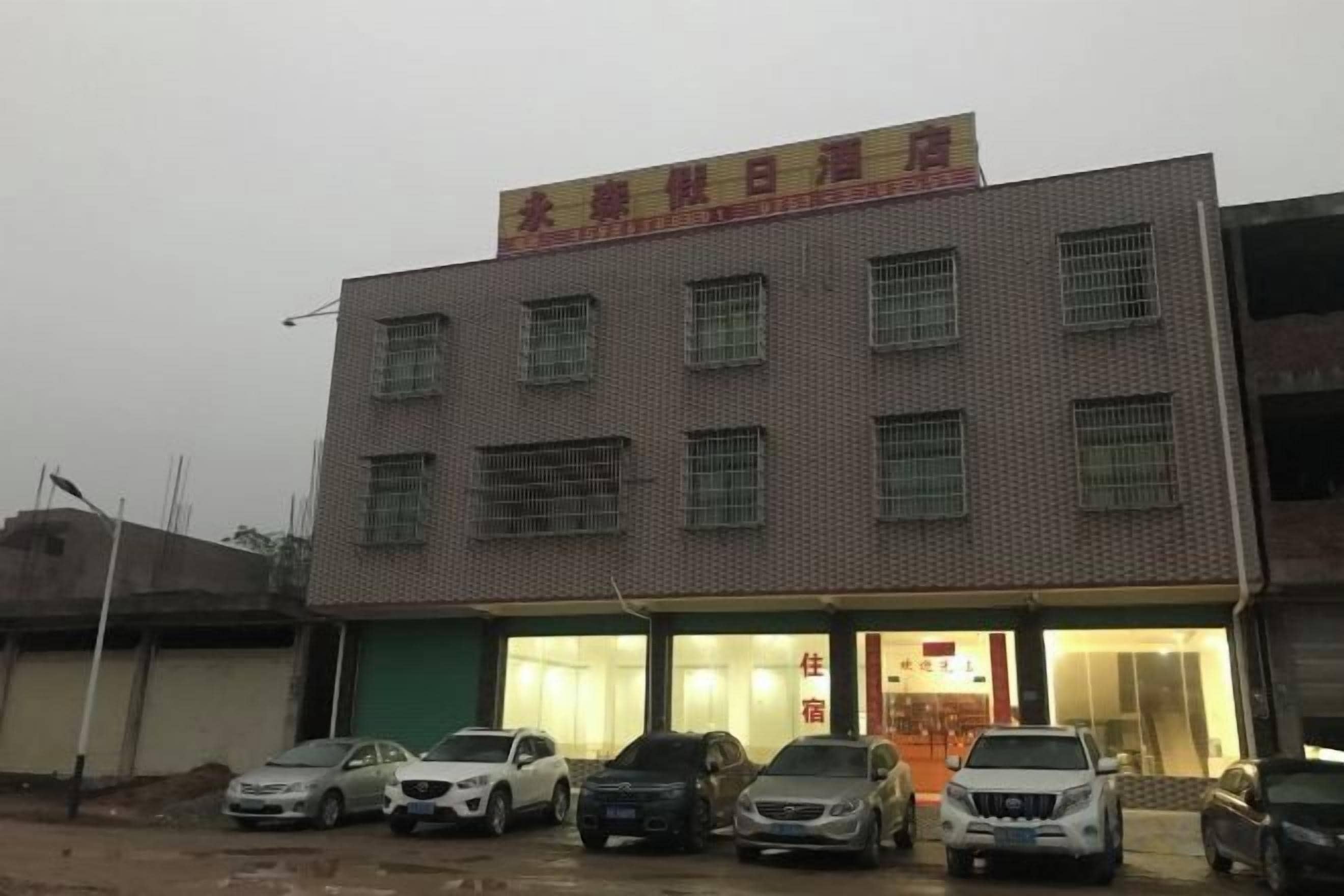 A building with multiple floors, a sign above the entrance, and several cars parked in front.