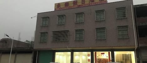 Um edifício com vários andares, uma placa sobre a entrada e vários carros estacionados em frente.