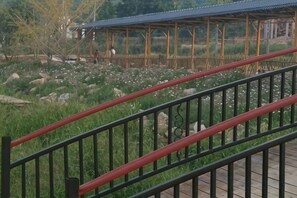 Un kiosque en bois surmonté d’un toit en métal, entouré d’une pelouse parsemée de rochers et de fleurs blanches.