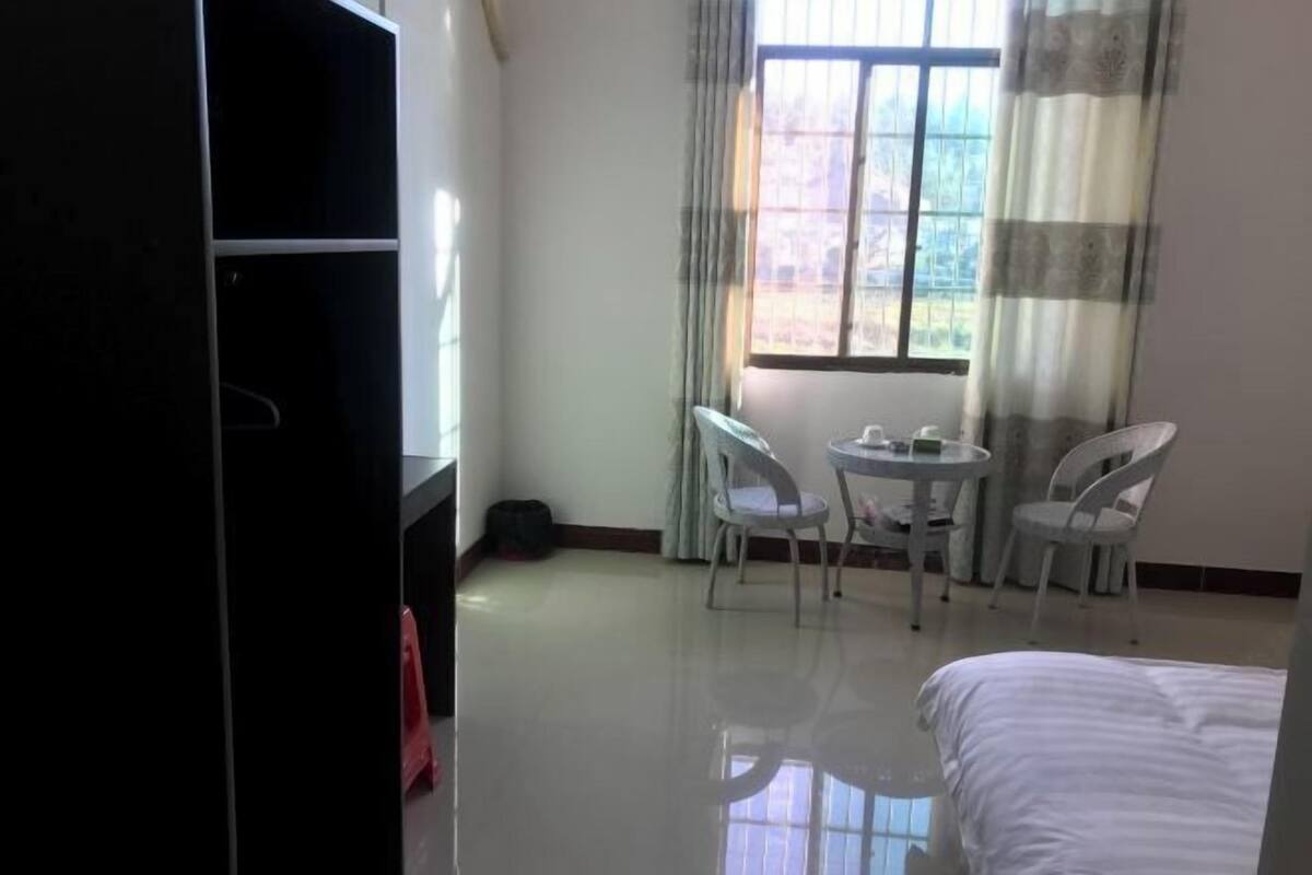 Une chambre d’hôtel avec un lit, une petite table avec des chaises, une fenêtre avec des rideaux et une armoire.