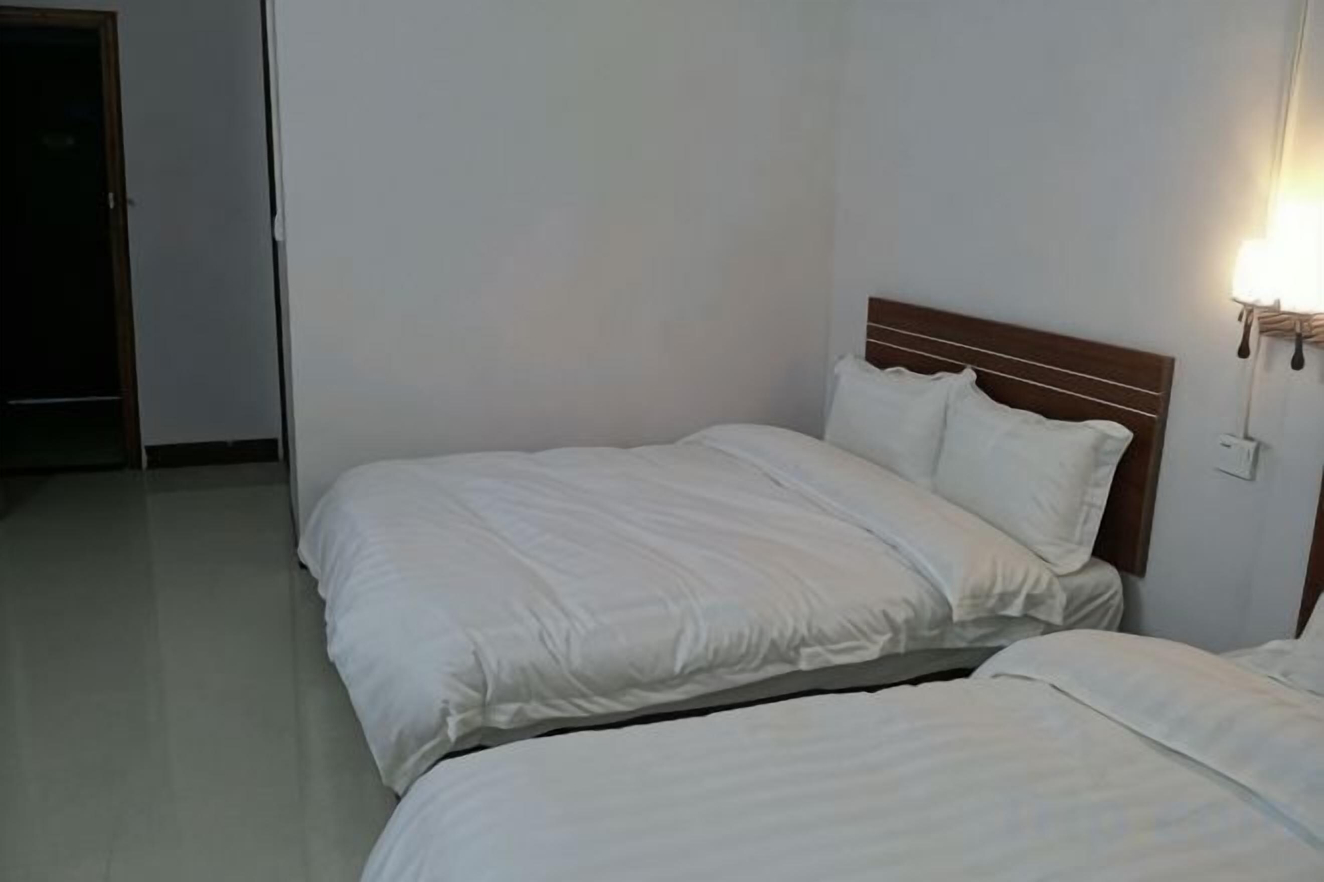 A hotel room with two beds, a wooden headboard, and a wall-mounted light fixture.