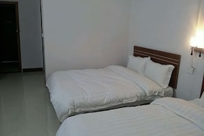 Habitación de hotel con dos camas, cabecera de madera y una lámpara fijada a la pared.