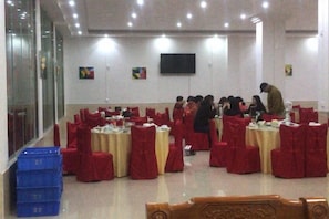 Un salón de conferencias con mesas redondas, sillas rojas y un televisor de pantalla plana en la pared.
