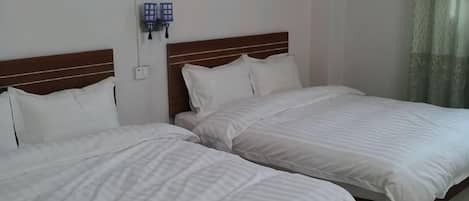 A hotel room with two single beds, a wooden headboard, a wall-mounted phone, and a window with curtains.