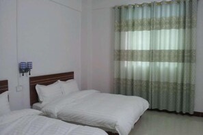 Habitación de hotel con dos camas individuales, cabecero de madera, cortina estampada y lámpara fijada a la pared.