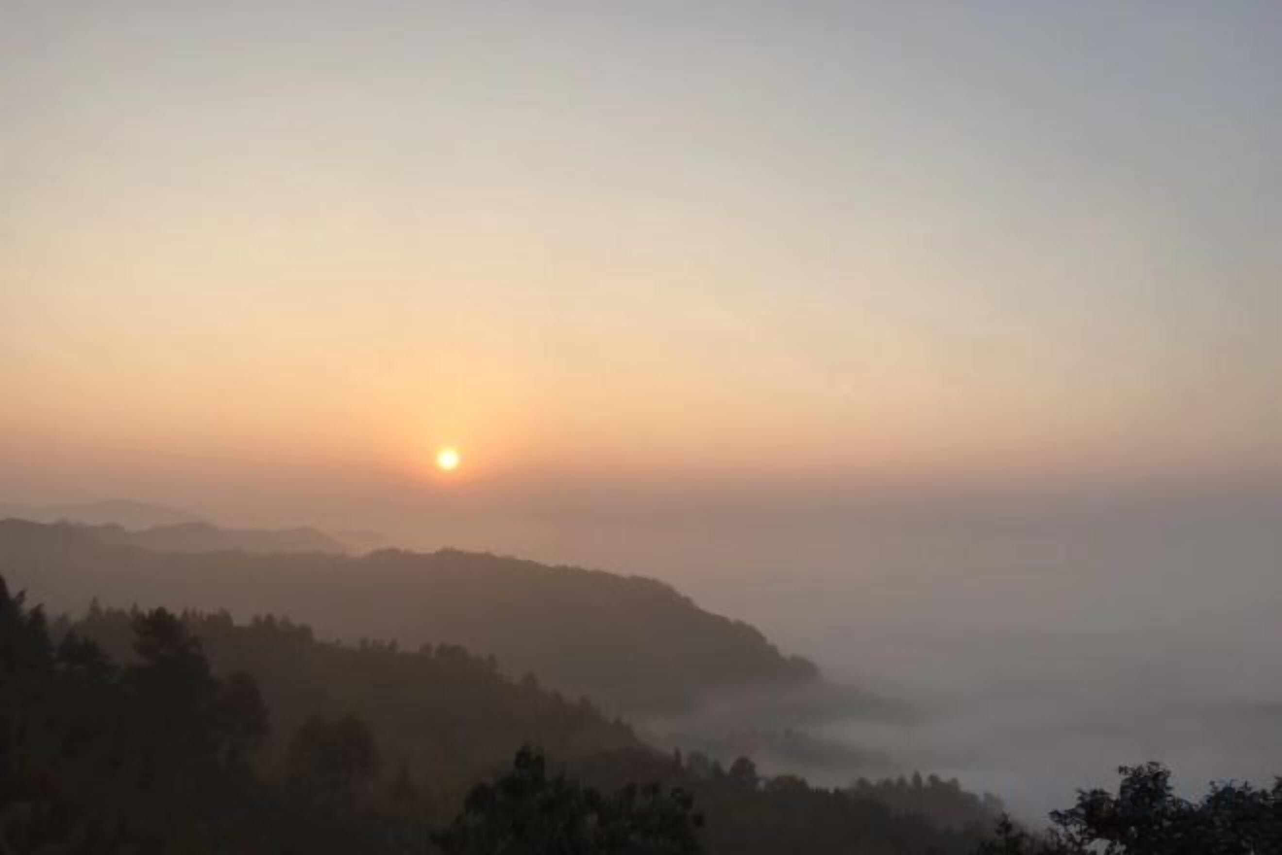 A sunrise over a misty landscape with hills in the distance.