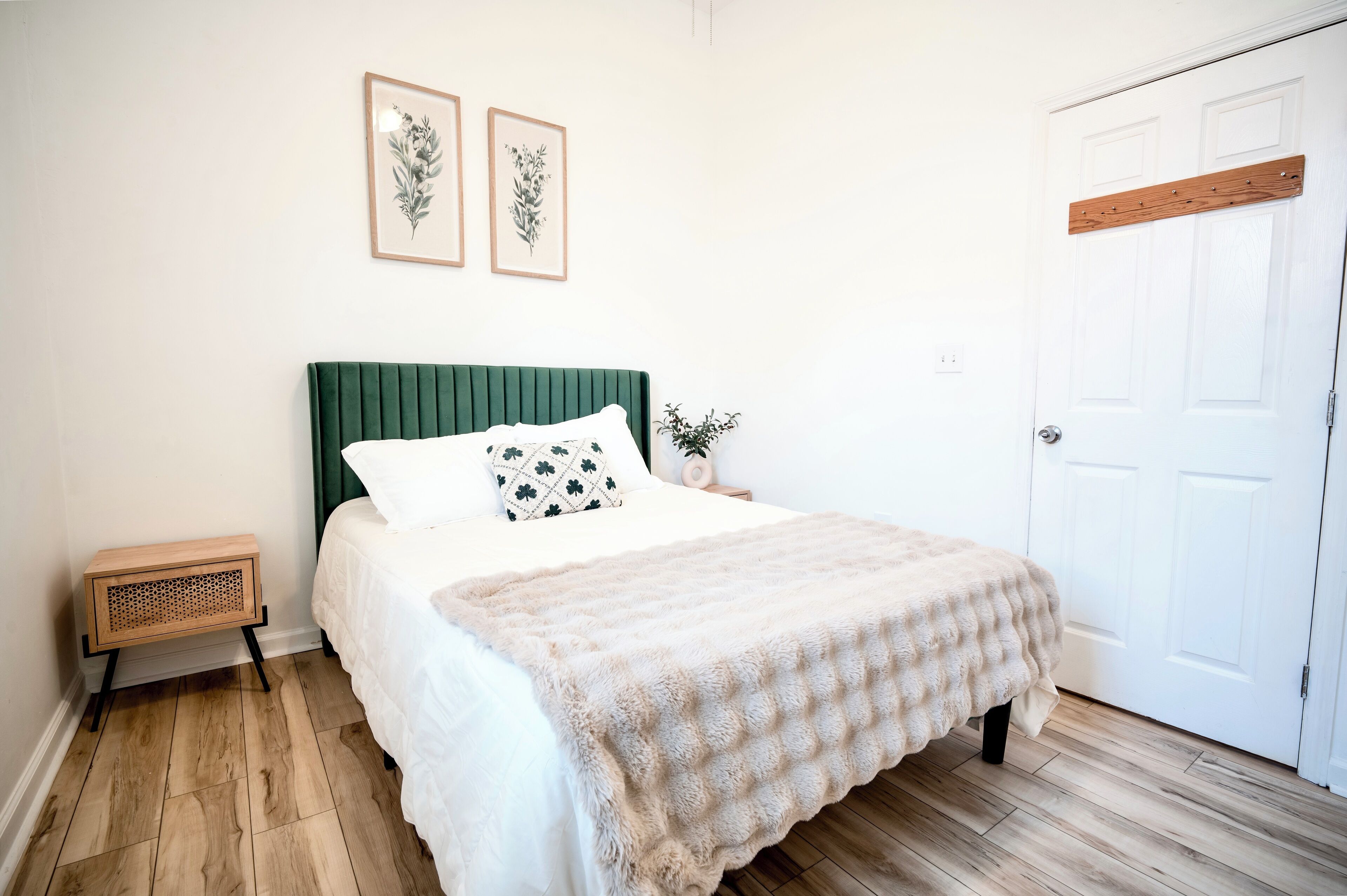 Un dormitorio ordenado con un cabecero tapizado en verde, una colcha blanca y una mesita de noche de madera.