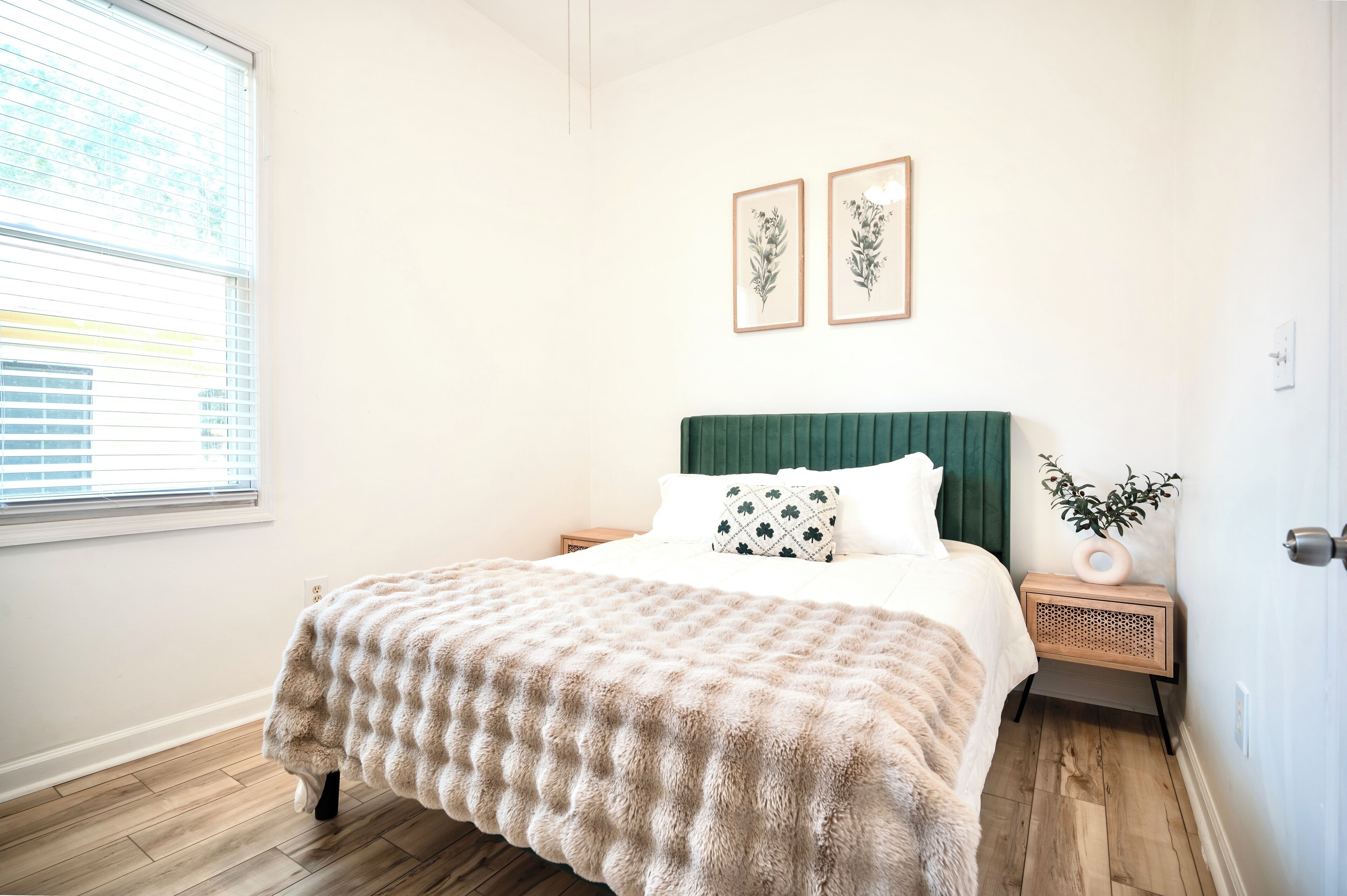 Ein Schlafzimmer mit einem Bett, einem Nachttisch, einem Fenster und zwei gerahmten Bildern an der Wand.