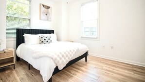Quarto com cama, mesa de cabeceira, obra de arte na parede e janela com persianas.