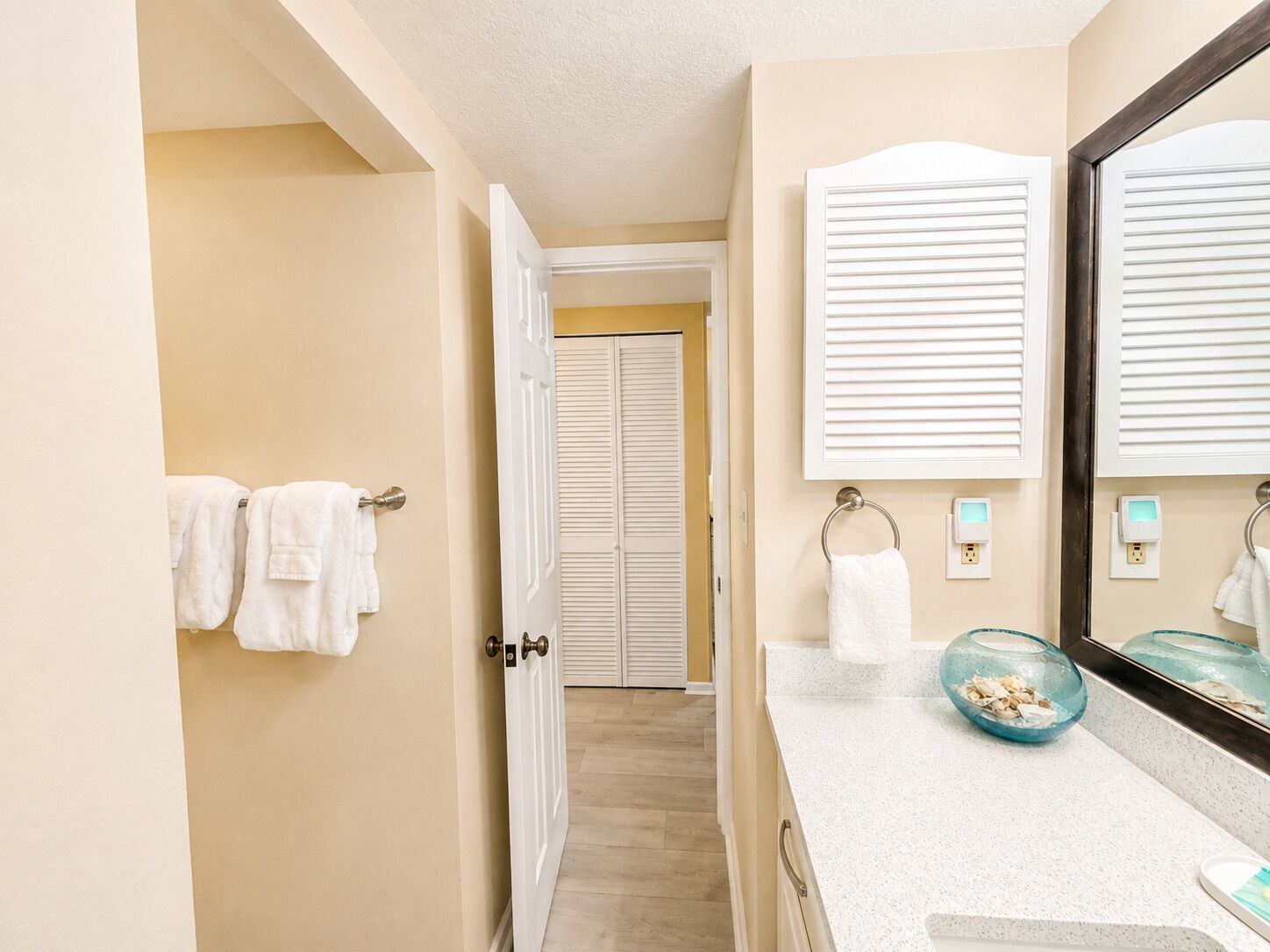 A hotel bathroom with a mirror, towel rack, and a bowl of toiletries.