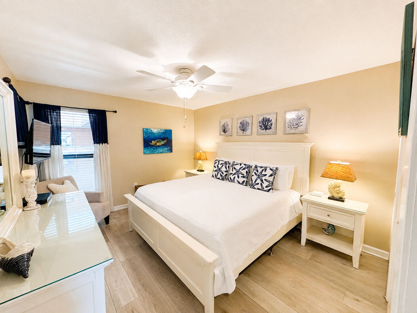 Ein Hotelzimmer mit Bett, Nachttischen, Deckenventilator, Wandbild und Blick ins Freie.
