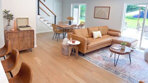 A spacious living area with a wooden floor, a leather sofa, a dining table with chairs, and a staircase leading to another level. - 5 Min to Downtown Warwick, Wineries, Breweries, Hikes, Shops, & Greenwood Lake! (Warwick)