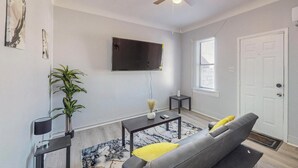 A living room with a grey sofa, a coffee table, a TV mounted on the wall, a ceiling fan, and a plant. - Charming 1-bedroom house in marvelous Albuquerque with WiFi, AC (albaquerque)