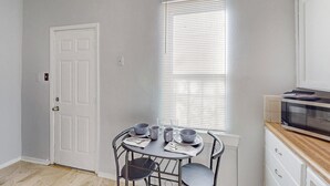 A small kitchen with a dining table set for four, a microwave, and a window with blinds. - Charming 1-bedroom house in marvelous Albuquerque with WiFi, AC (albaquerque)