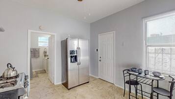 A compact kitchen with a stainless steel refrigerator, a gas stove, and a dining table with chairs.