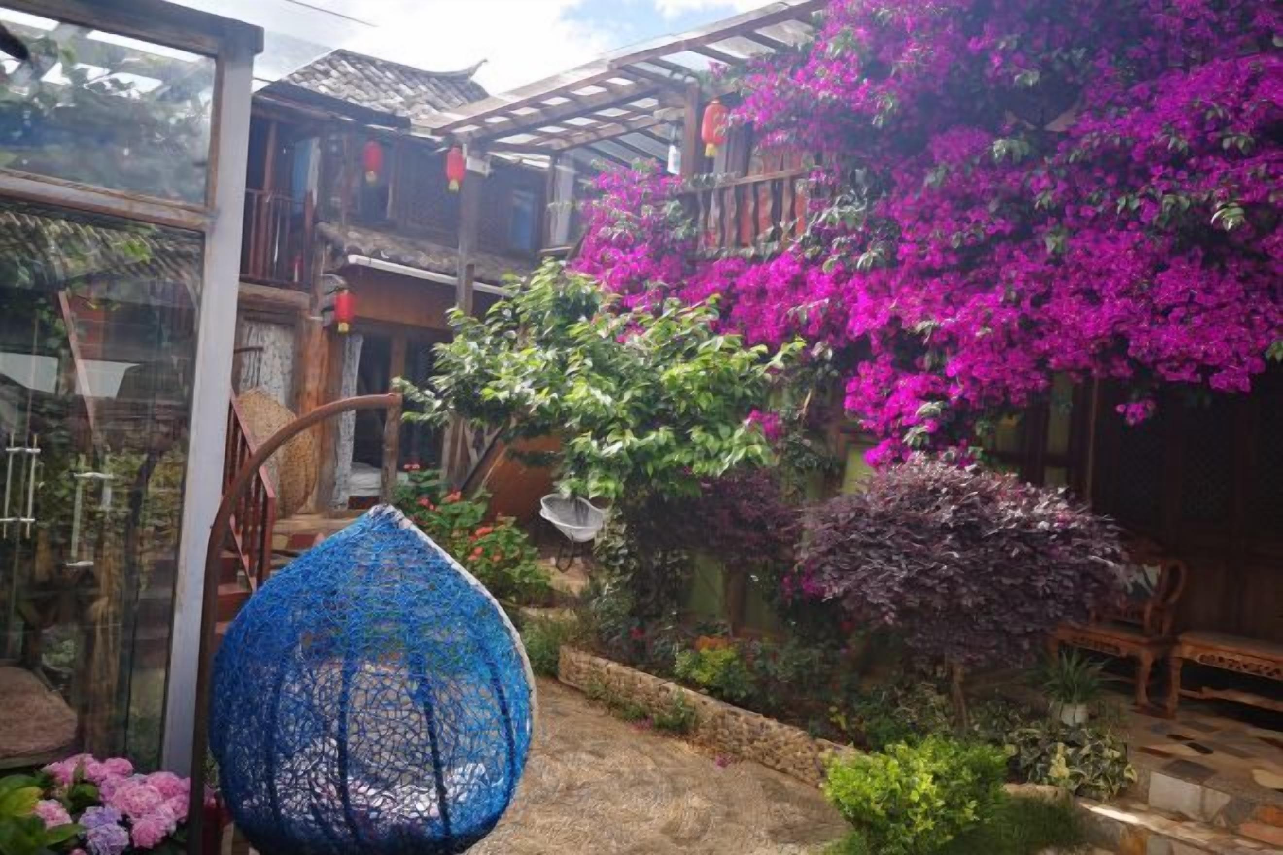 A traditional wooden house with a balcony, a blue lace chair, and vibrant pink bougainvillea flowers.