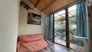 A room with a wooden ceiling, a pink bean bag chair, a white table, and a large window with curtains.