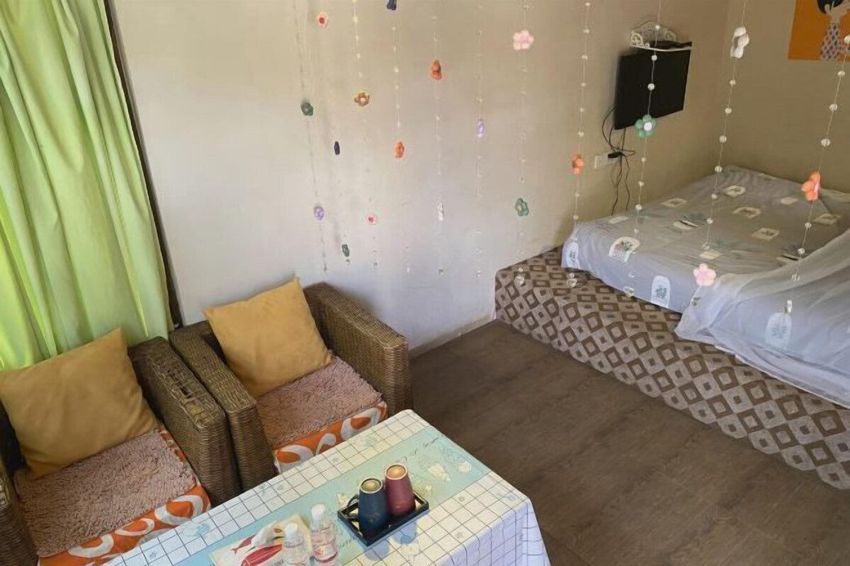 A room with a sofa, a table with bottles, a patterned bed, and a wall with hanging decorations.
