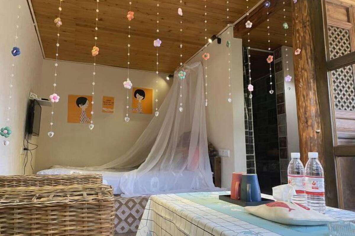 Una habitación con una cama, un mosquitero, una cesta de mimbre y una mesa con botellas de agua.