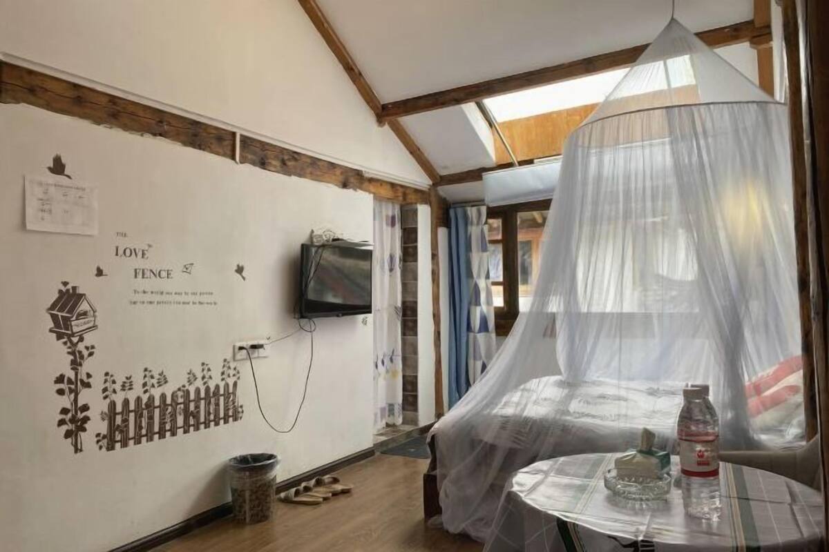 Una habitación con cama bajo un dosel, una mesa con una botella y una pared con una ilustración de una valla.