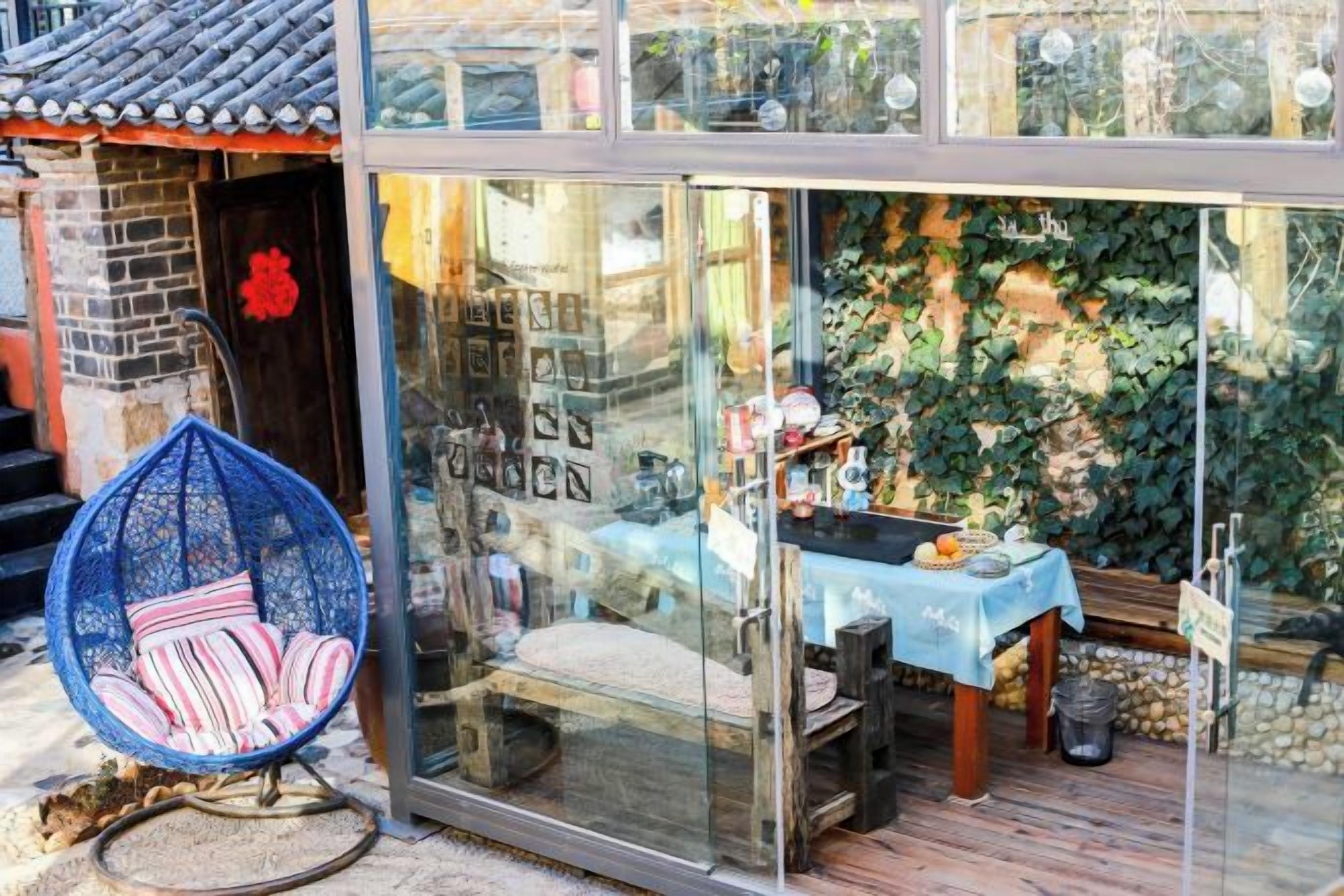 A glass-fronted shop with a blue tablecloth, a wicker chair, and a wooden deck.