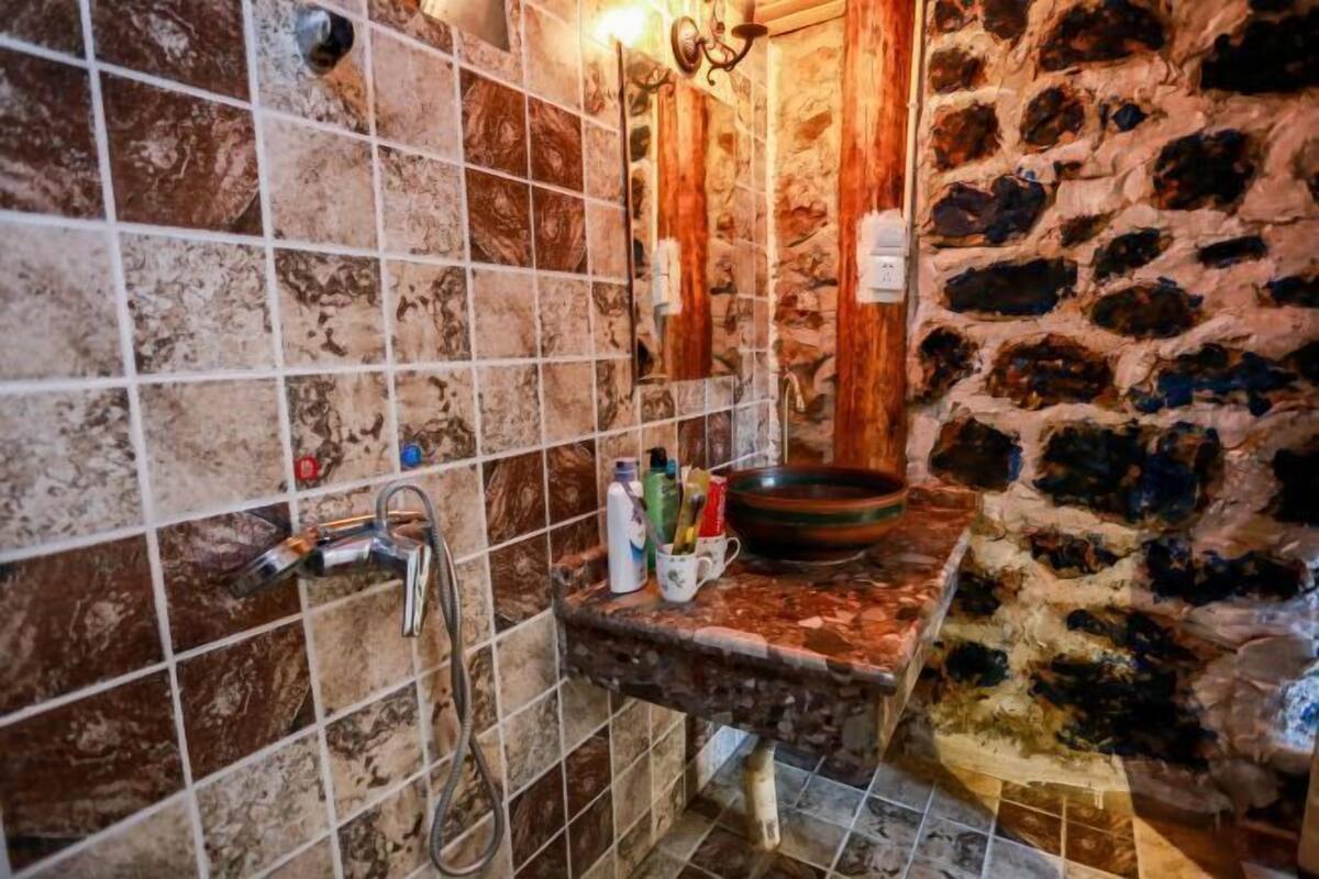 Un baño con pared de azulejos, un lavamanos con artículos de aseo y una pared de piedra.
