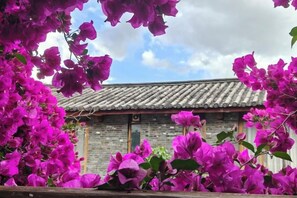 A traditional building with a tiled roof and wooden doors, surrounded by vibrant purple flowers. - Lijiang Youmi Inn (Lijiang)