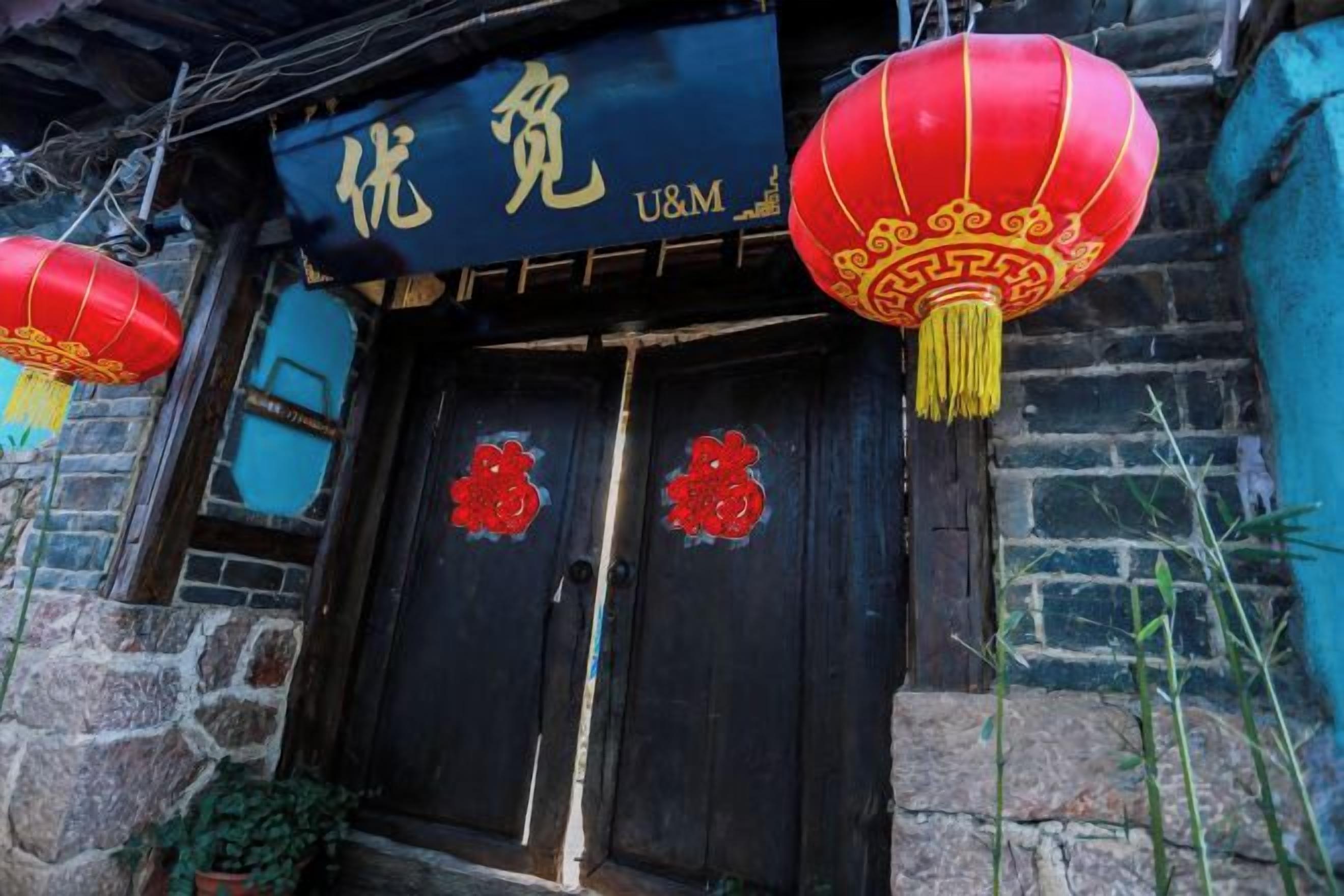 A traditional building with a dark wooden door, red lanterns, and a sign with Chinese characters.