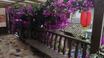Un balcón de madera con suelo de baldosas, baranda de madera y flores moradas.