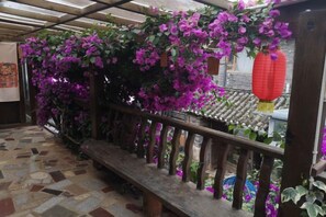 A wooden balcony with a tiled floor, a wooden railing, and purple flowers. - Lijiang Youmi Inn (Lijiang)
