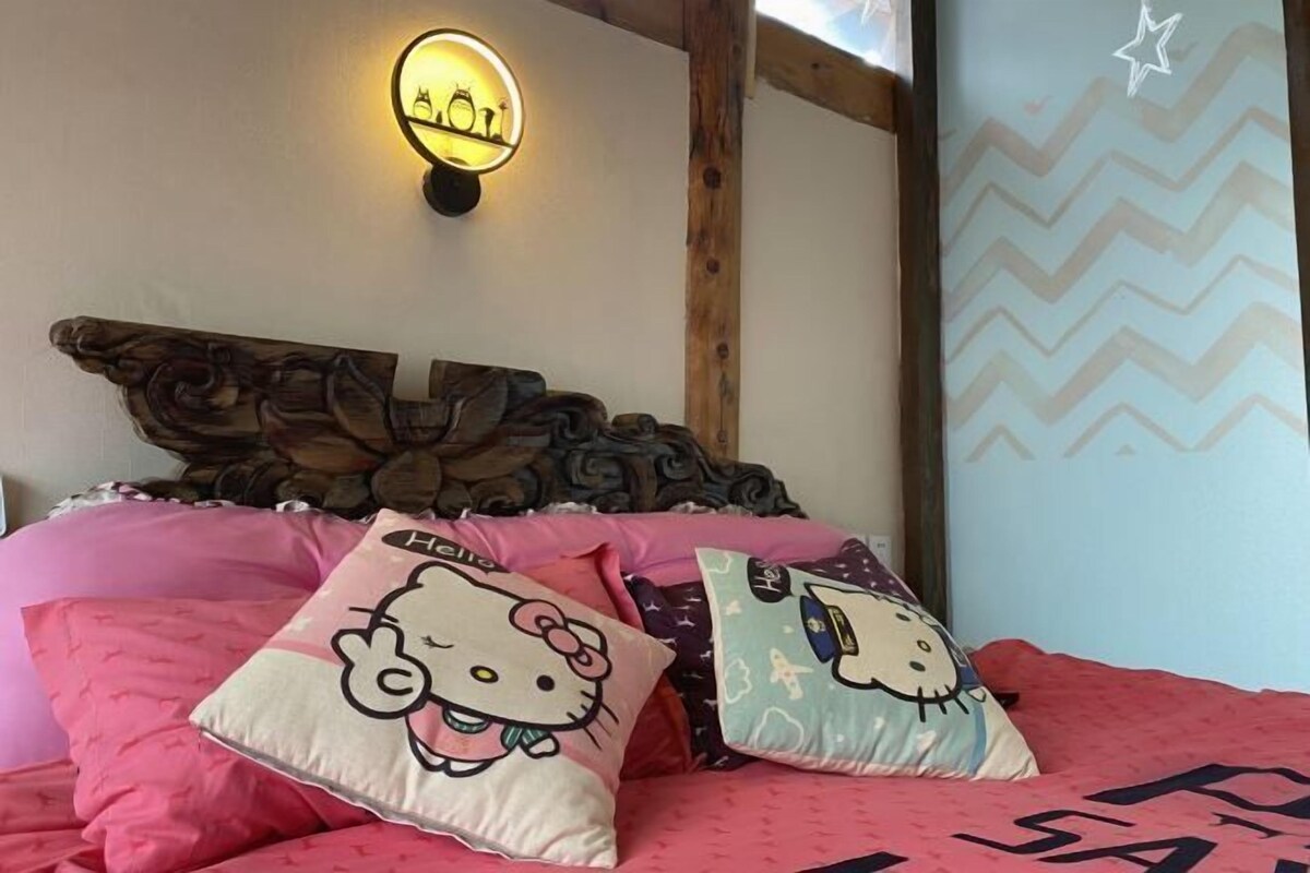 A bed with Hello Kitty pillows, a wooden headboard, and a wall light.