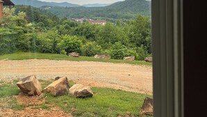 A view through a window of a landscape with a grassy area, large rocks, and distant hills. - Nacoochee 3, Cozy cabin, close to town, walking trails, winery, adventures  (Helen)