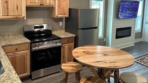 A modern kitchen with granite countertops, wooden cabinets, stainless steel appliances, and a round wooden table with stools. - Nacoochee 3, Cozy cabin, close to town, walking trails, winery, adventures  (Helen)