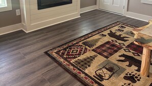 A living room with a flat-screen TV mounted on a white wall, a fireplace below, and a patterned rug on the floor. - Nacoochee 3, Cozy cabin, close to town, walking trails, winery, adventures  (Helen)