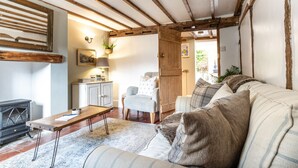 A cozy living room with a fireplace, wooden beams, a sofa, a chair, and a small table. - Poppy Cottage - Cosy 2BD Home, Perfect For Family (Clifford Chambers)