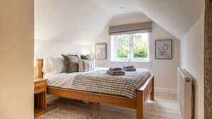 A bedroom with a wooden bed, a bedside table, a window with a view of greenery, and two wall art pieces. - Poppy Cottage - Cosy 2BD Home, Perfect For Family (Clifford Chambers)