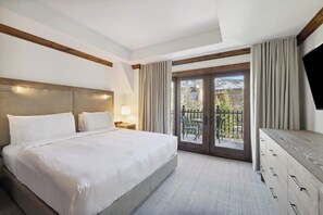 Ein Hotelzimmer mit einem großen Bett, einem hölzernen Kopfteil, einem Fernseher, einem Schminktisch und einem Balkon mit Blick auf ein Gebäude und Bäume.