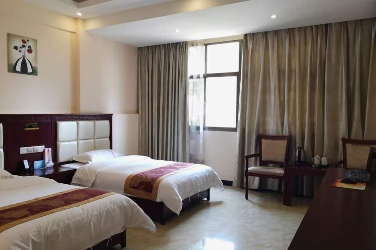 Habitación de hotel con dos camas, un escritorio, una silla y un ventanal con cortinas.