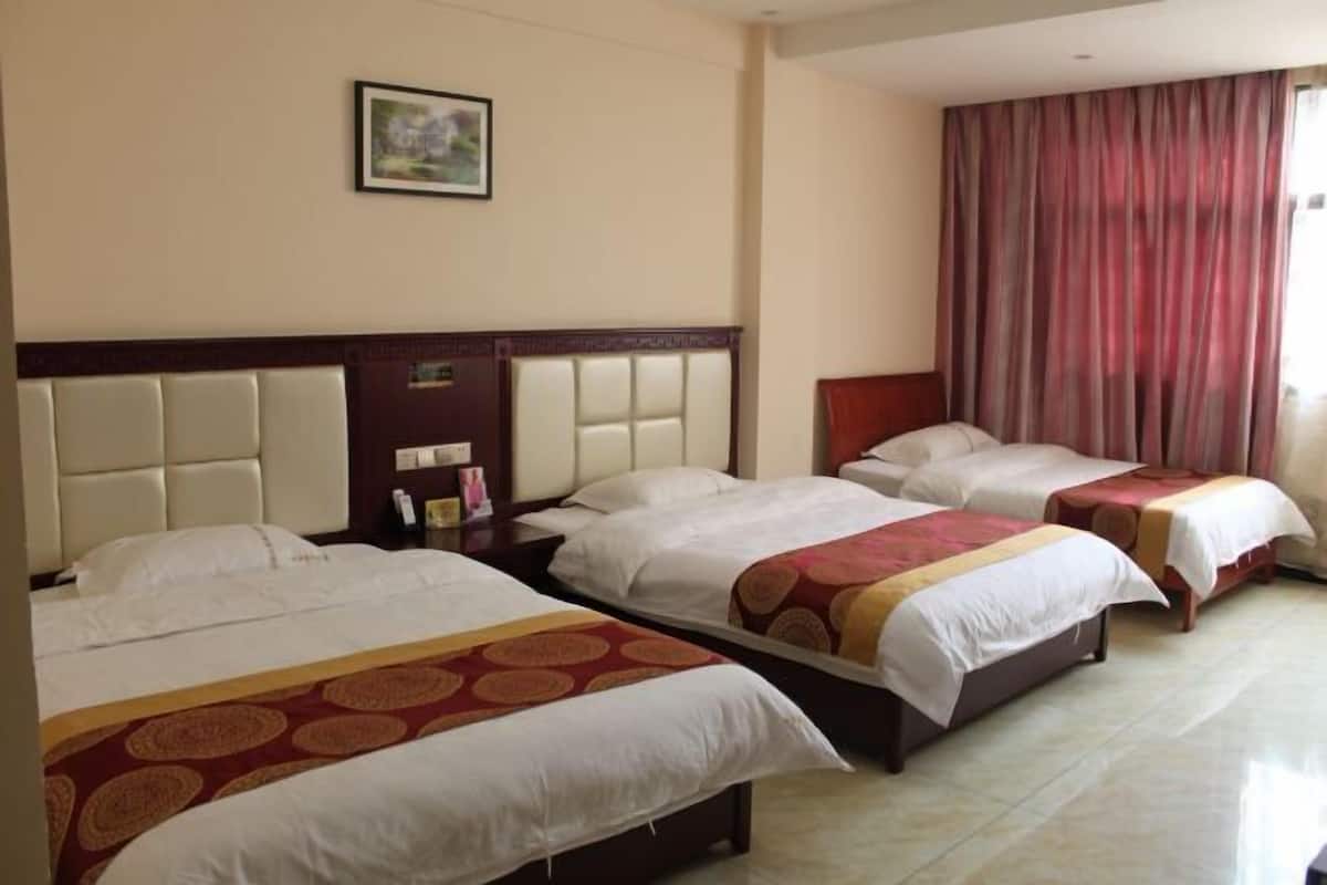 Habitación de hotel con tres camas, cabecero, mesita de noche, un cuadro en la pared y ventana con cortinas.